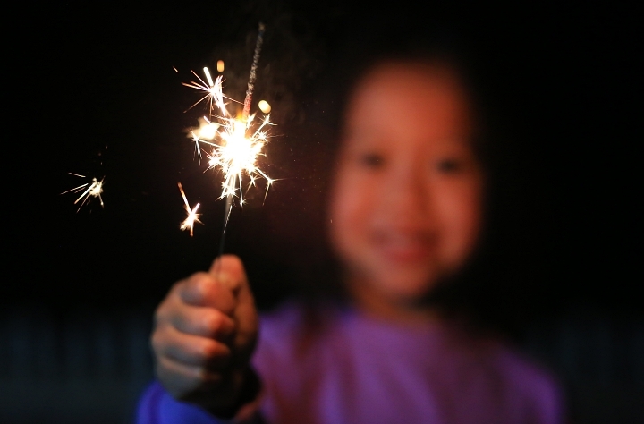 A small out of focus girl holds a Fourth of July sparkler