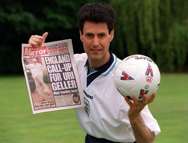 Uri Geller holding a soccer ball in one hand and a tabloid in the other